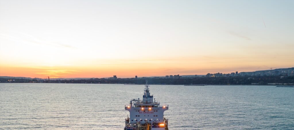 Cargo blanc au mouillage dans un port industriel, vue panoramique au coucher de soleil avec skyline urbaine